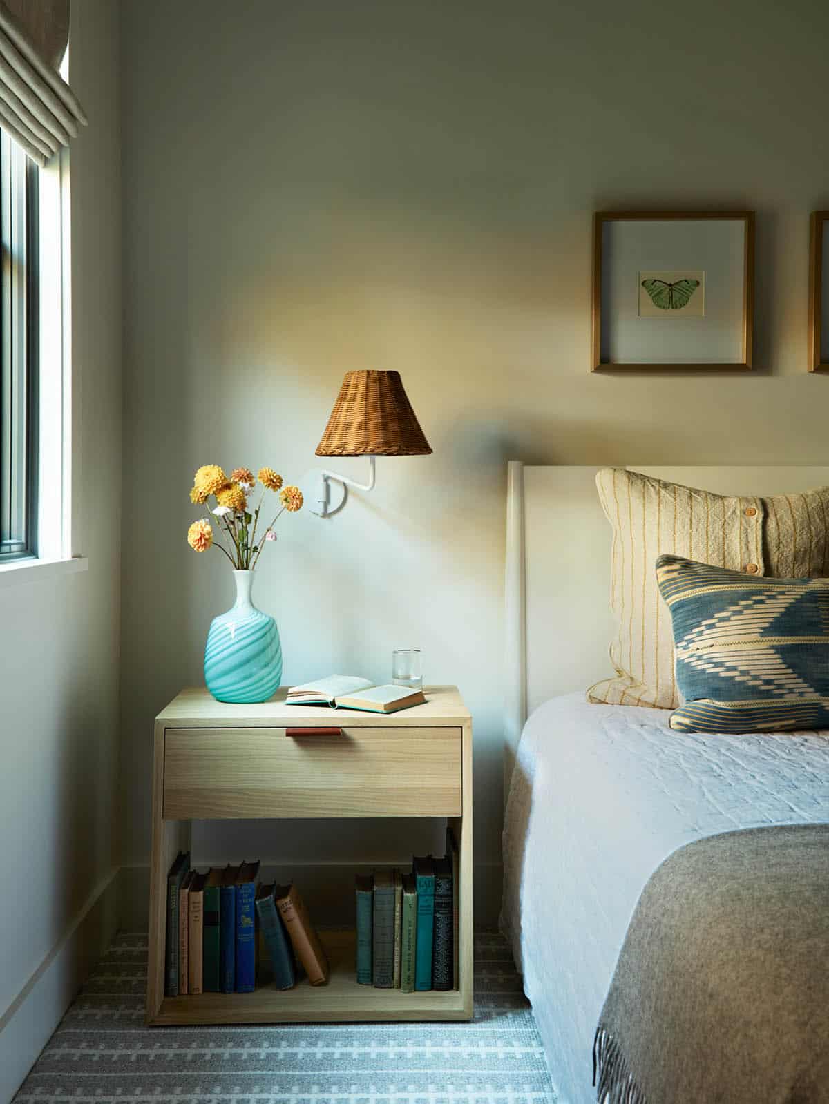 Bedside table styled with a ceramic vase and rattan wall sconce