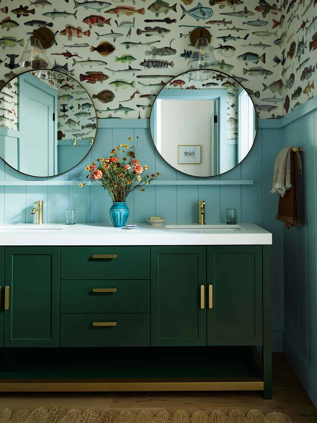 Bathroom vanity with fish print wallpaper and round brass mirrors