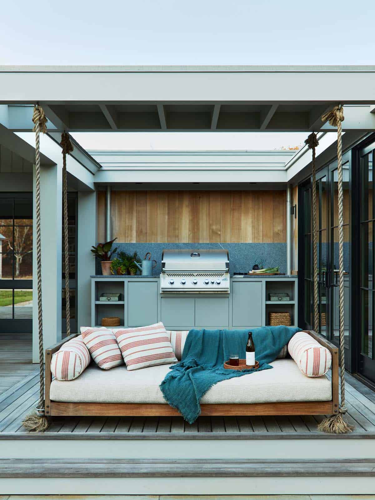 Hanging daybed swing facing an outdoor kitchen with a built-in grill
