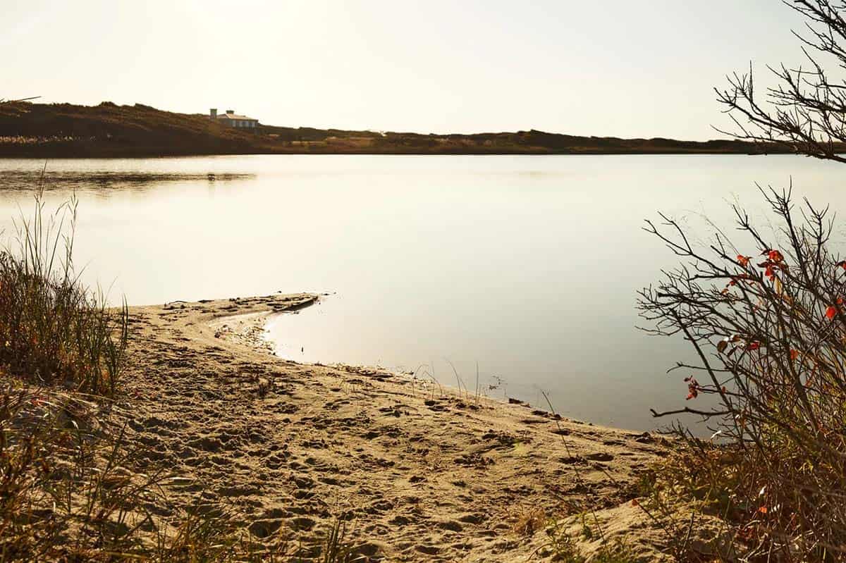 Sandy salt pond shoreline with the home visible across the water