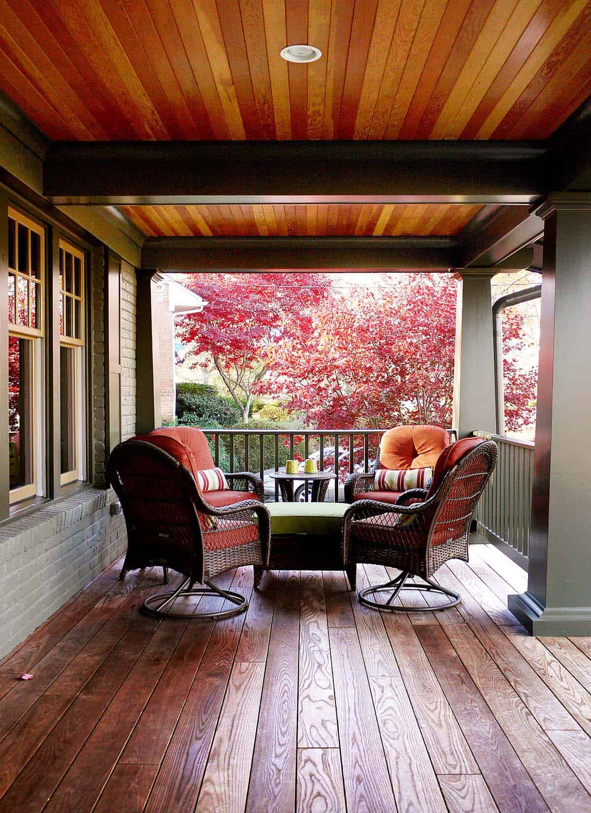 Covered deck with swivel wicker chairs, orange cushions, and rich wood ceiling