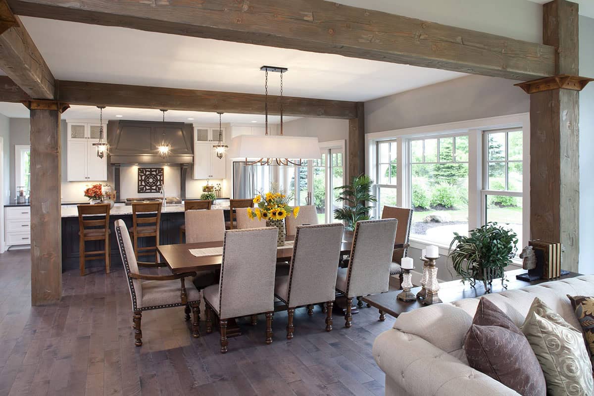 Open-concept dining and living area with reclaimed wood beams, dark wood table, and upholstered chairs