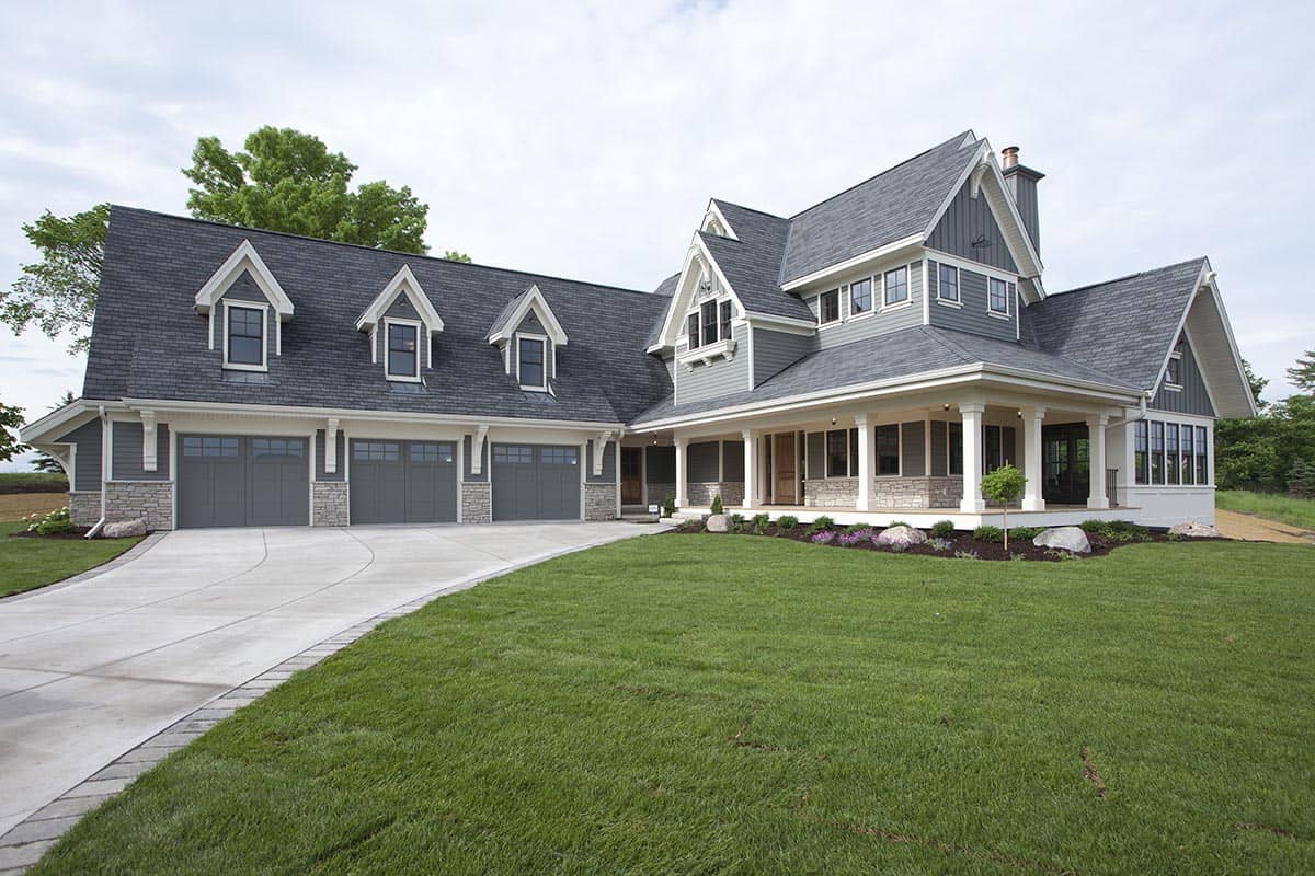 Craftsman-style home exterior with three-car garage, stone accents, and wraparound covered porch