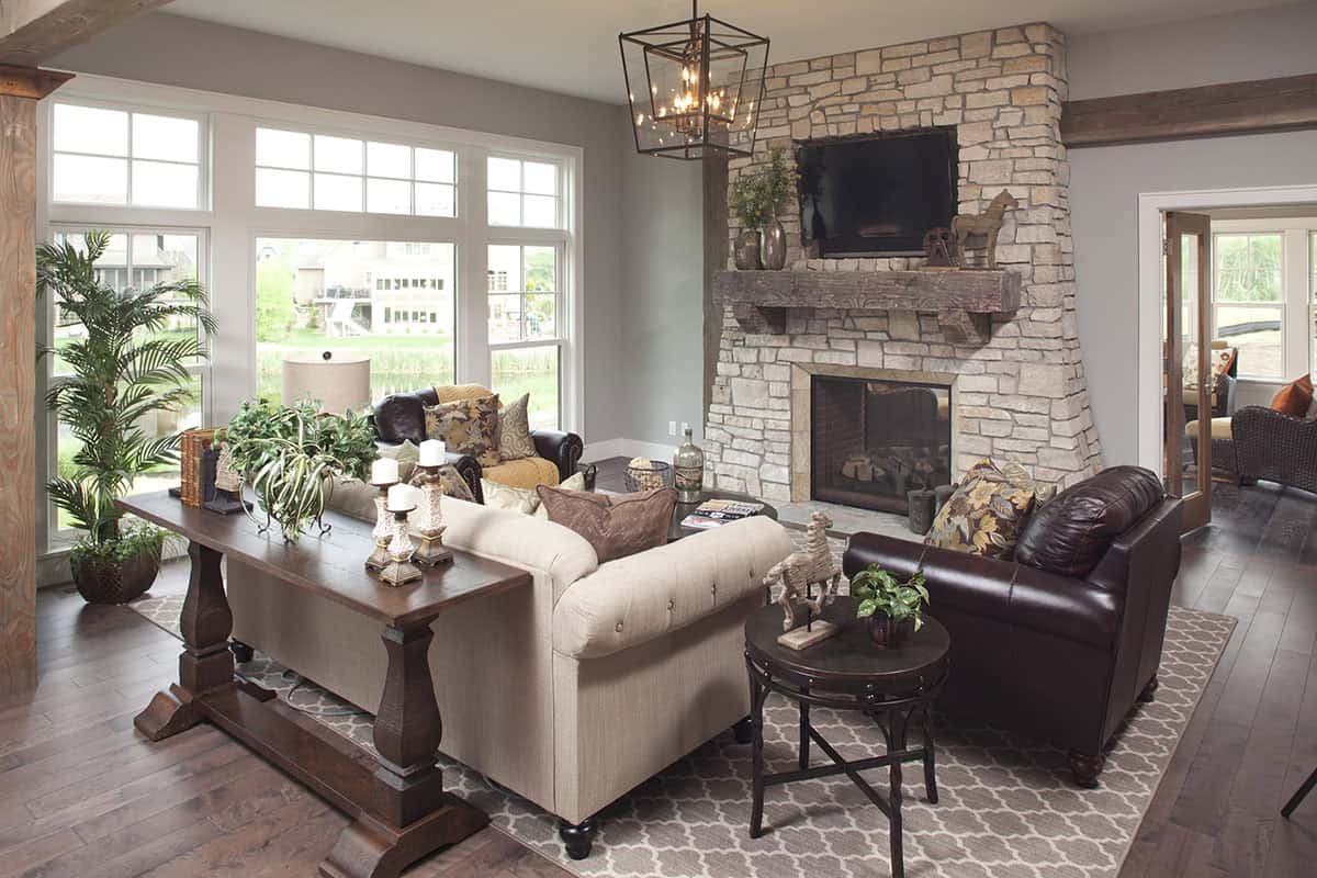 Living room with stone fireplace, wood mantel, leather armchairs, and beige tufted sofa