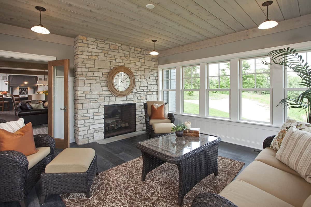 Sunroom with stone fireplace, wicker furniture, and shiplap ceiling with pendant lights