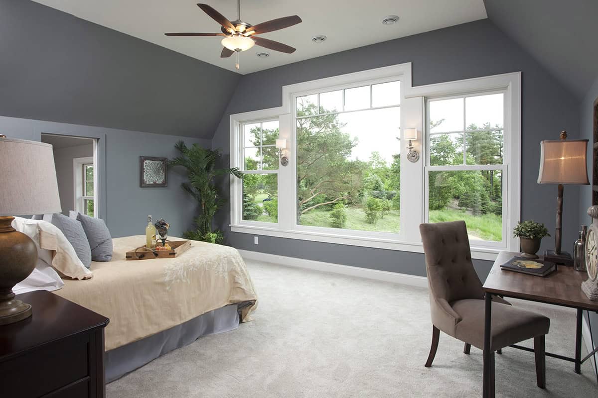Bedroom with vaulted gray ceiling, large windows, ceiling fan, and upholstered desk chair