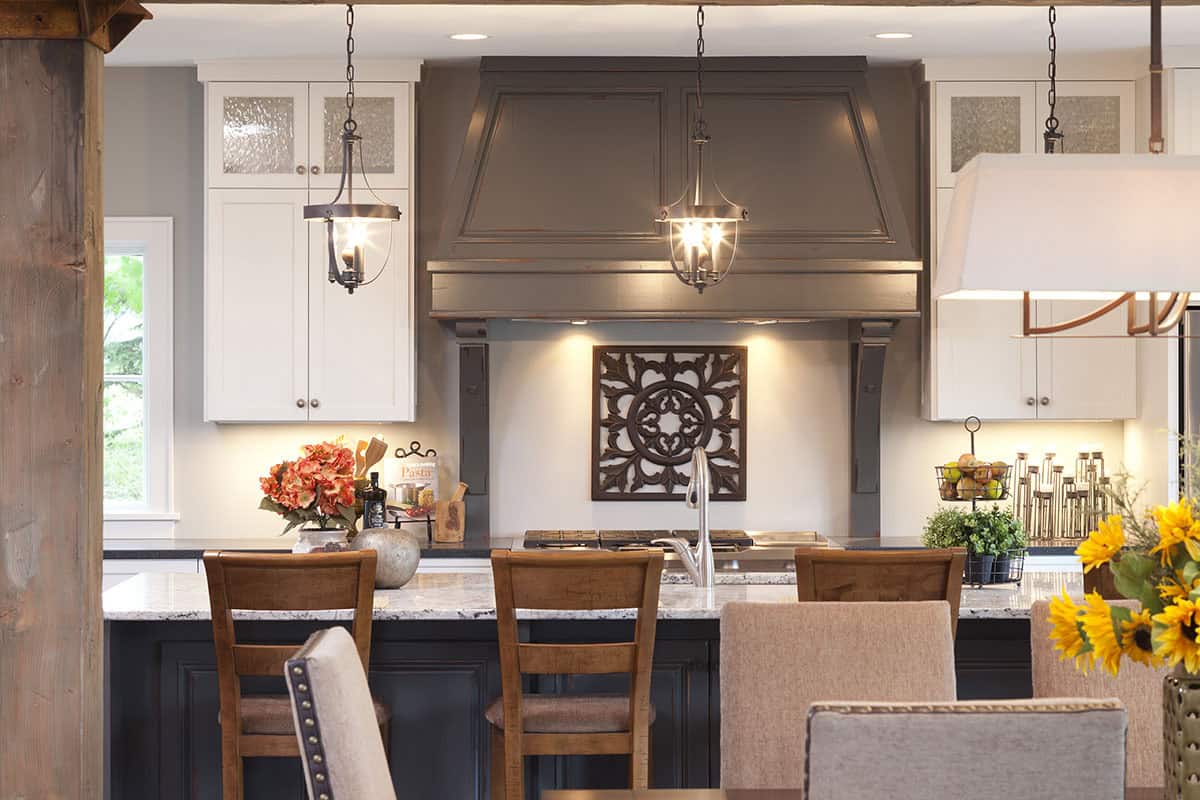 Kitchen range hood detail with gray paneled hood, pendant lights, and decorative iron wall art