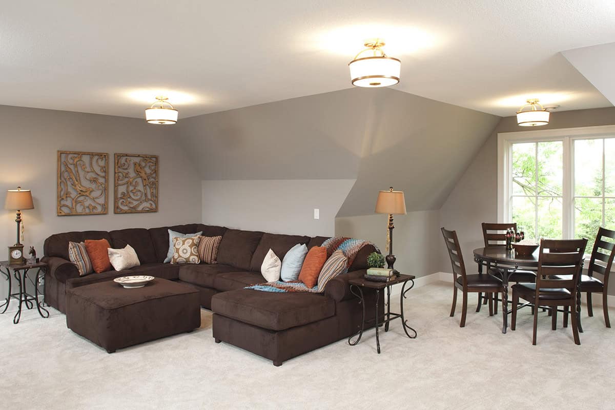 Family room with brown sectional sofa, sloped ceiling, and round dining table by window