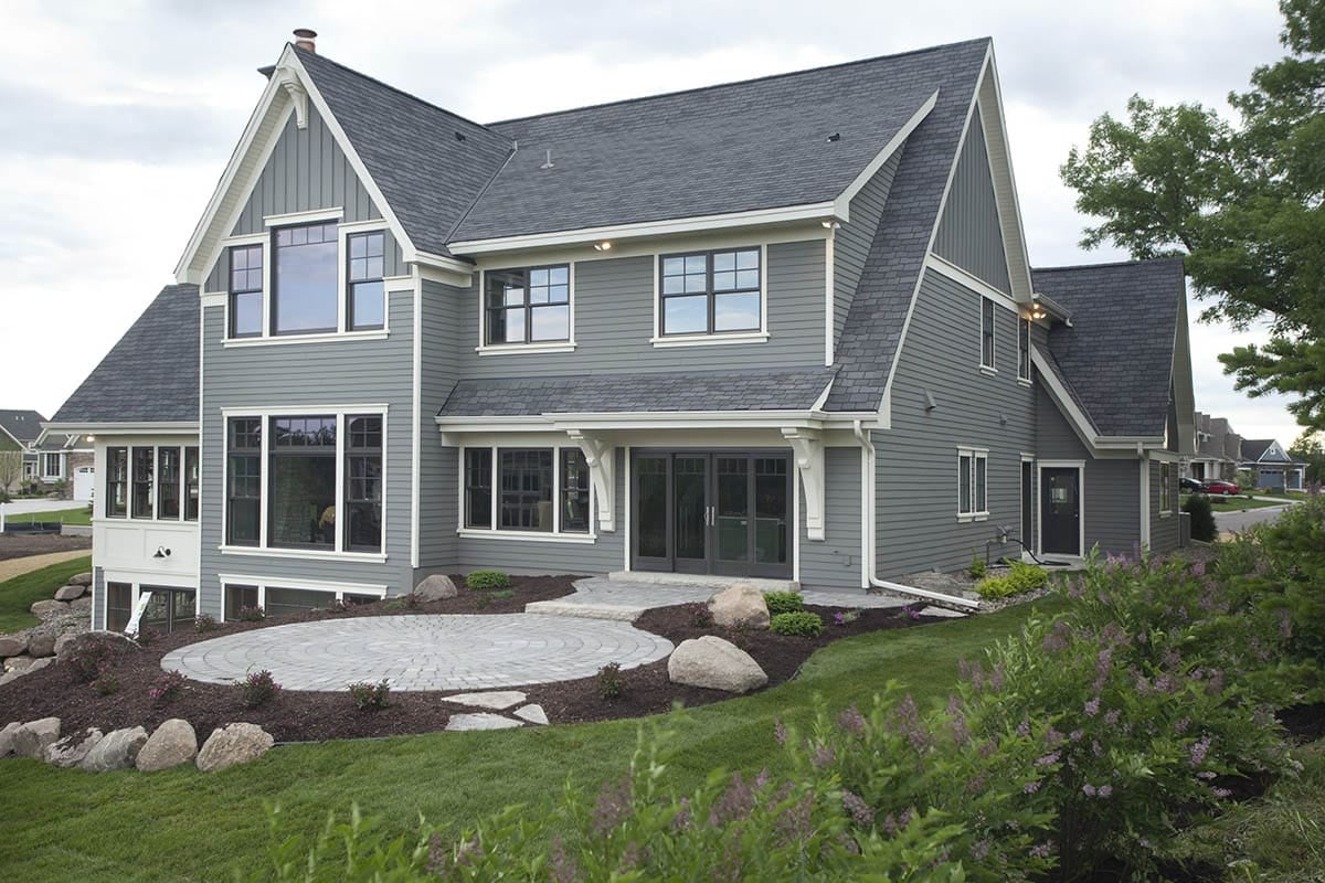 Rear exterior of home with covered patio, stone paver seating area, and landscaped yard