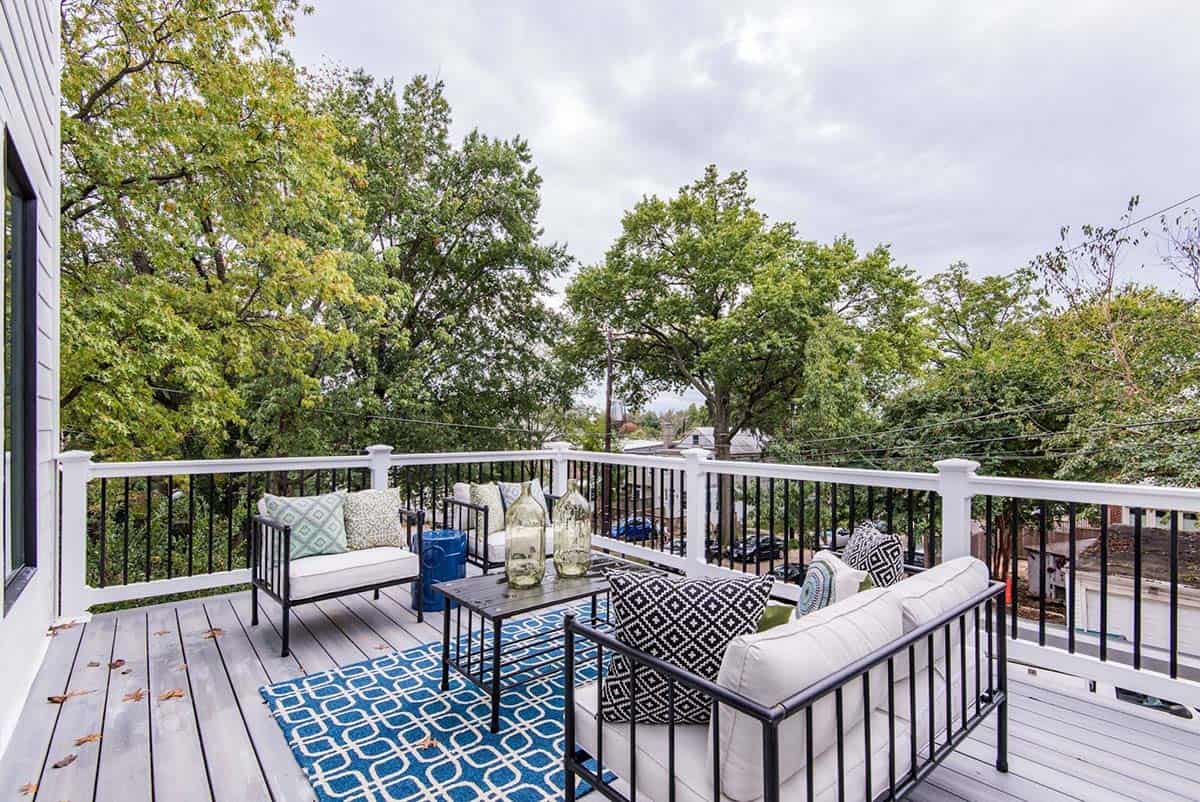 Rooftop deck with black metal furniture, white cushions, and blue patterned outdoor rug