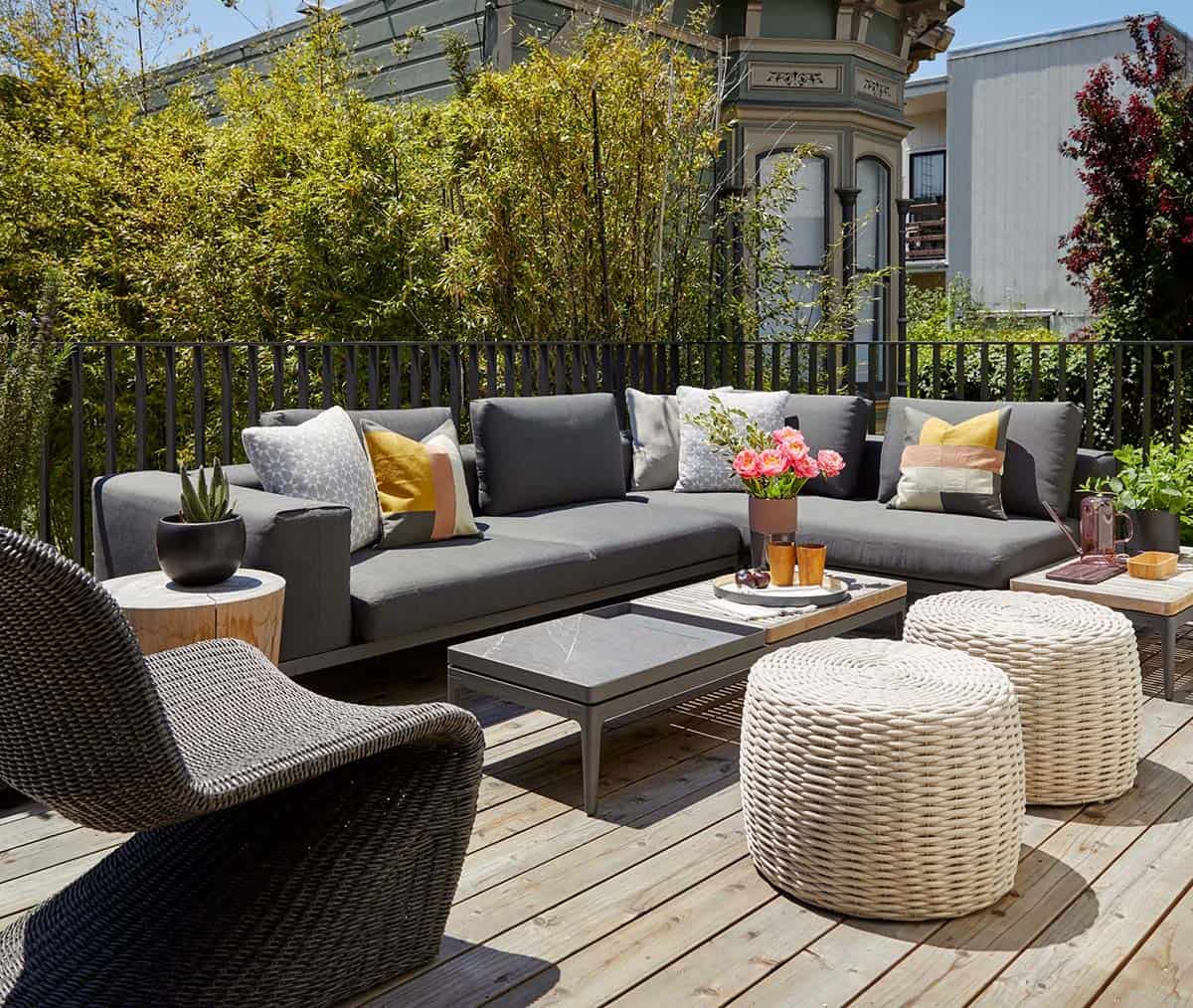 Deck lounge area with charcoal sectional sofa, woven poufs, and mixed-material coffee tables