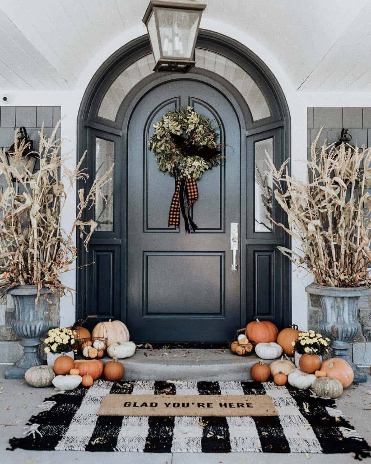 Arched front door with cornstalk urns and pumpkins on a striped rug