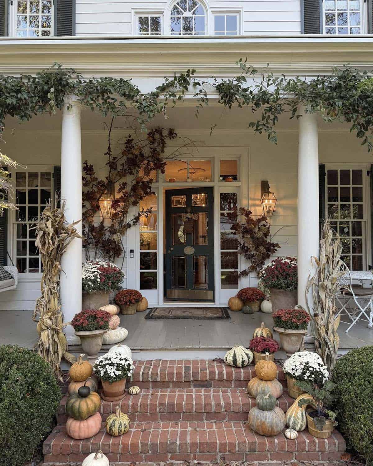 Front porch with cornstalks, mums and stacked pumpkins on brick steps