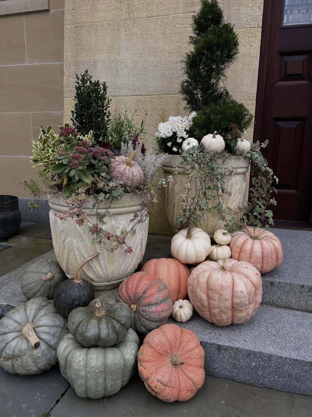 Front steps with a pile of dusty pink and sage pumpkins by stone urns