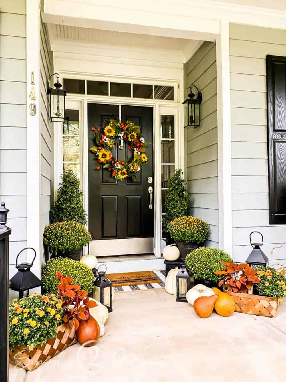 Black front door with sunflower wreath, mums and gourds on the porch