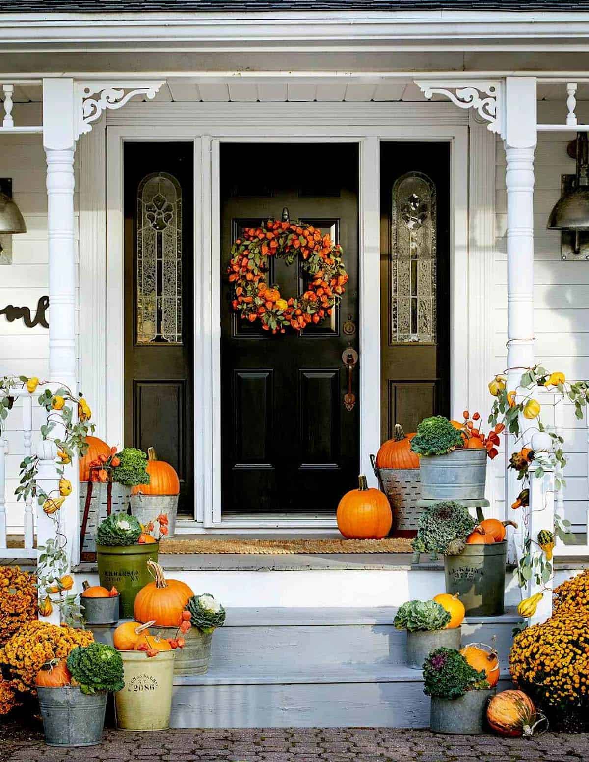 Front porch steps lined with galvanized buckets of pumpkins and kale