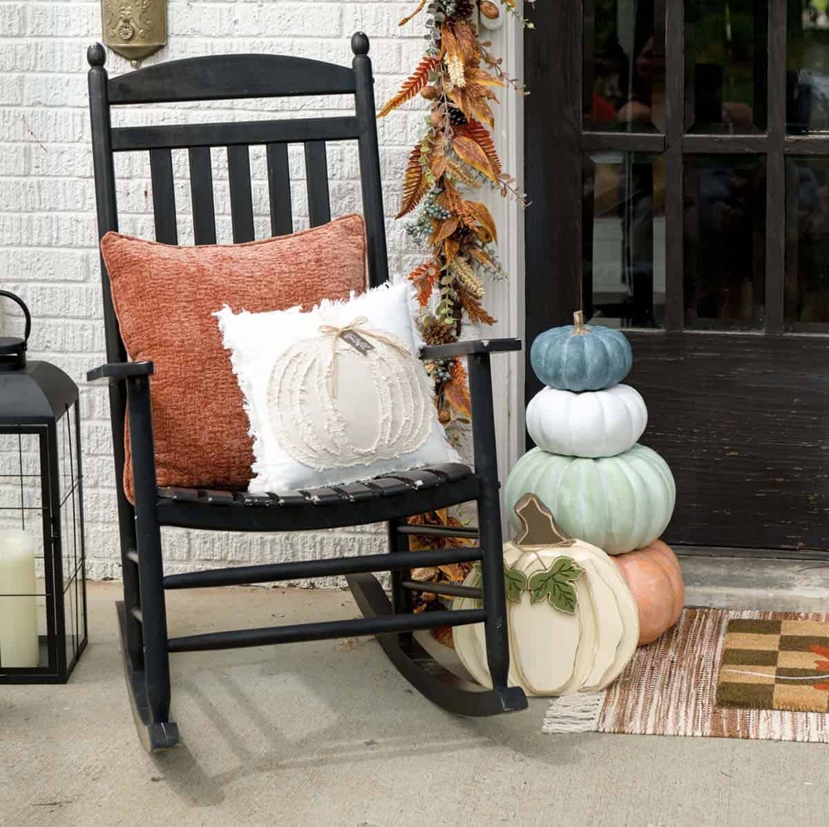 Black rocking chair with pumpkin pillows beside a stacked pumpkin display