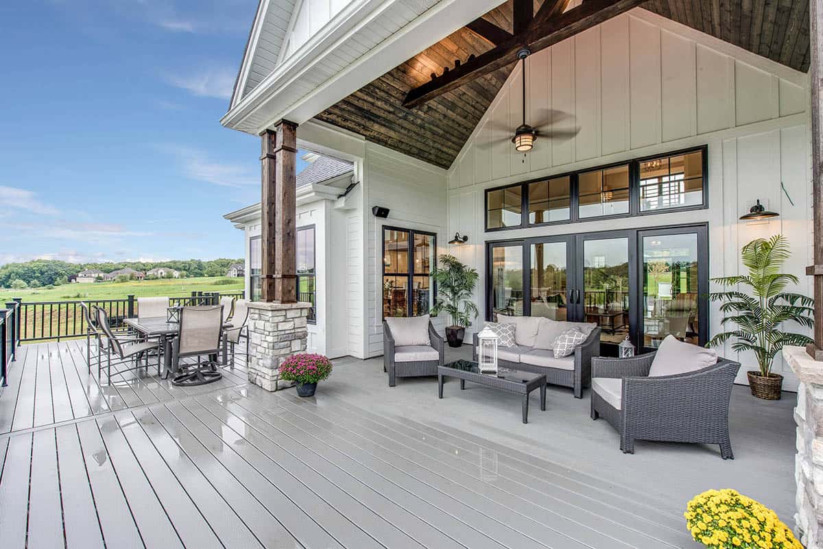 Farmhouse-style covered deck with vaulted wood beam ceiling, gray wicker furniture, and ceiling fan