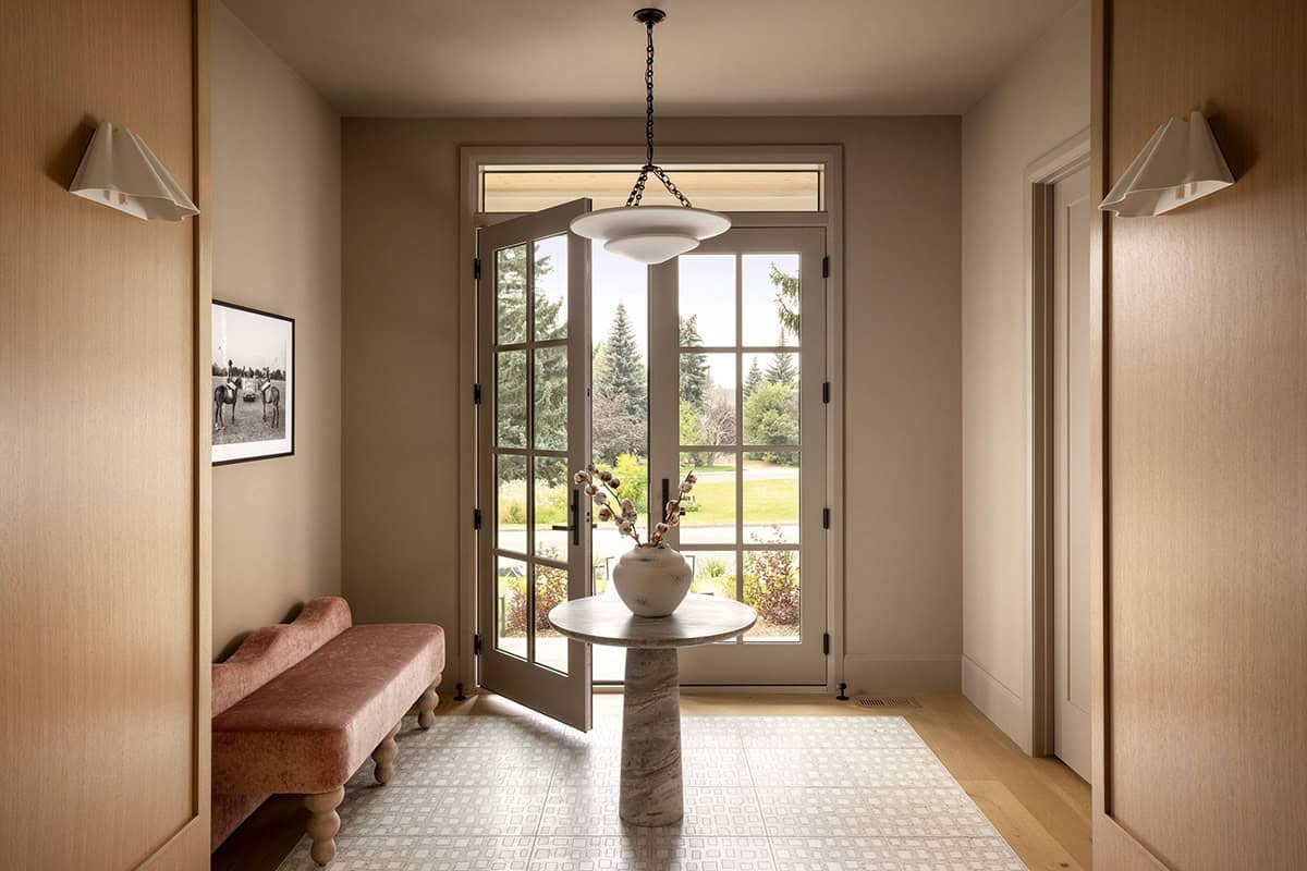 Entryway with black French doors, pink bench, and round marble table on patterned tile floor