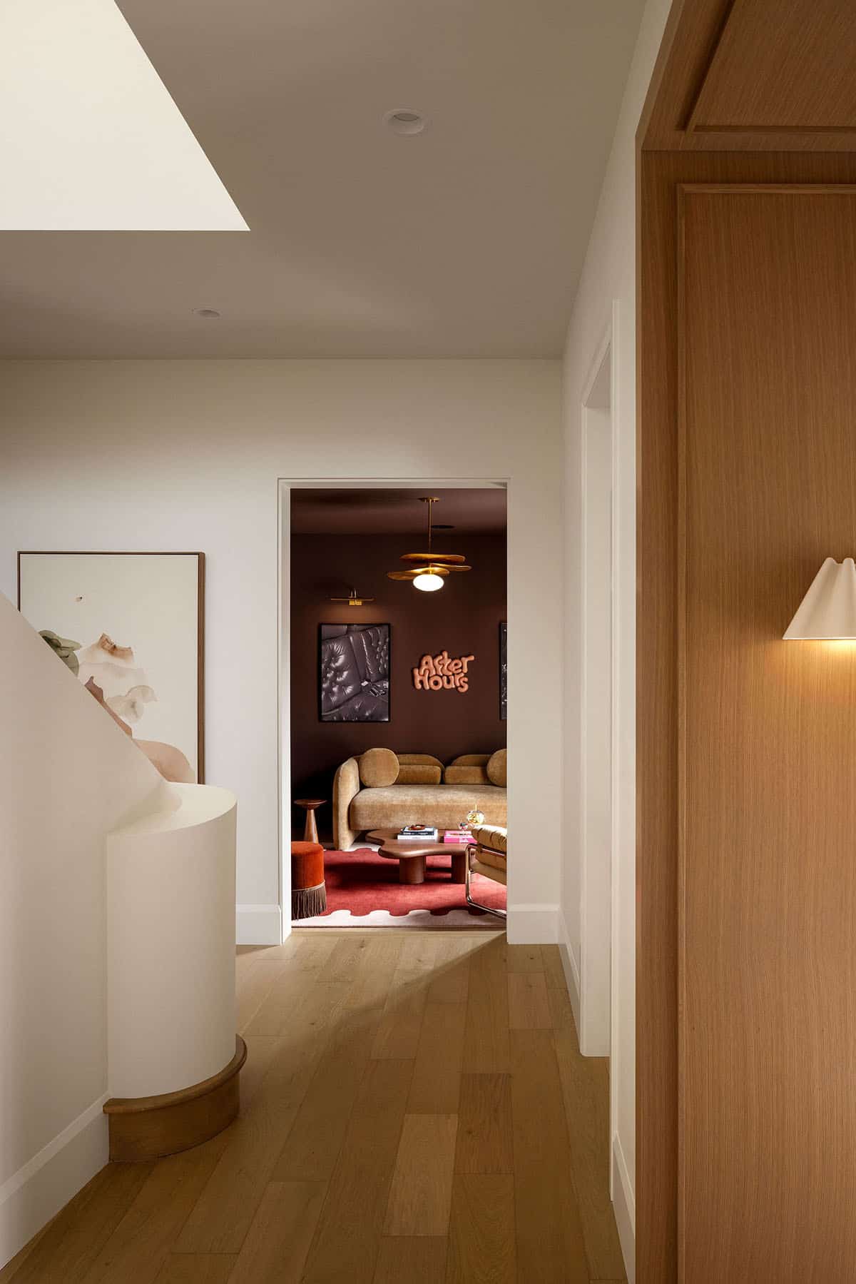 Hallway view into a dark lounge with "After Hours" wall art and curved sofa