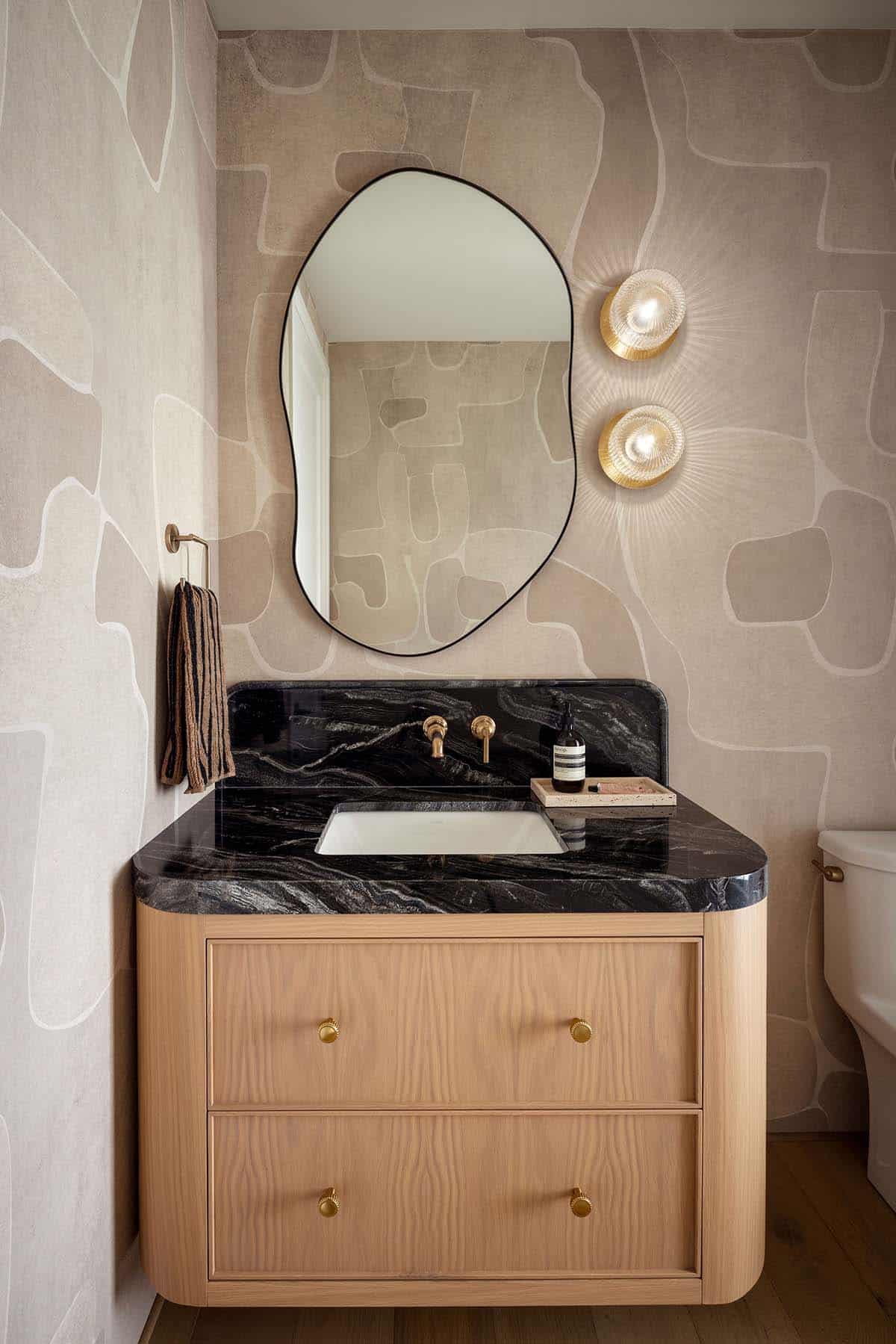 Powder room with organic-shaped mirror, black marble vanity, and scalloped brass sconces