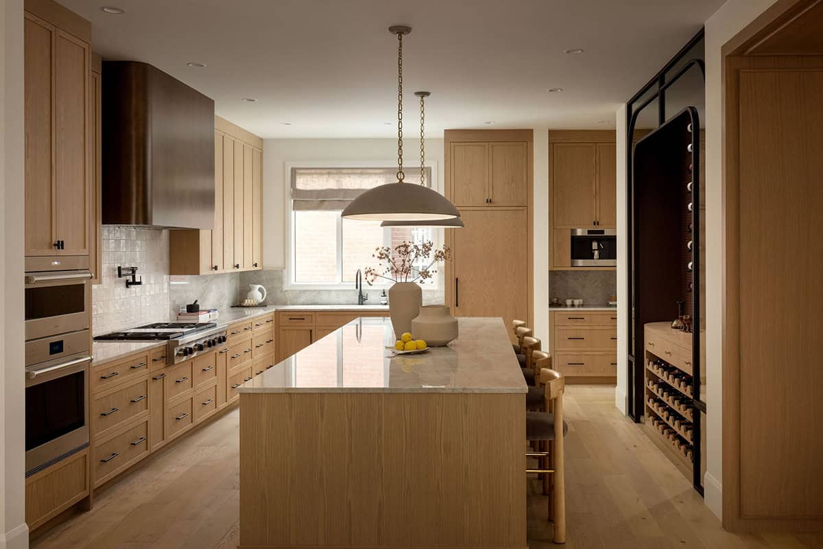Kitchen with oak cabinetry, dark metal range hood, and dome pendant lights over island