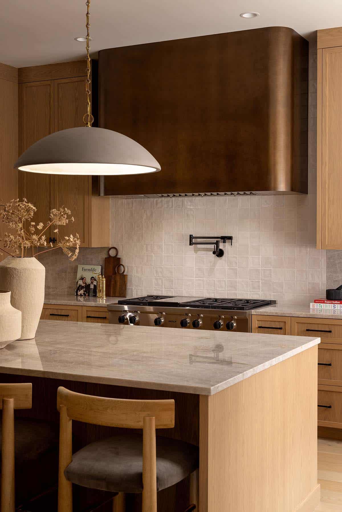 Close-up of kitchen range with curved bronze hood and zellige tile backsplash