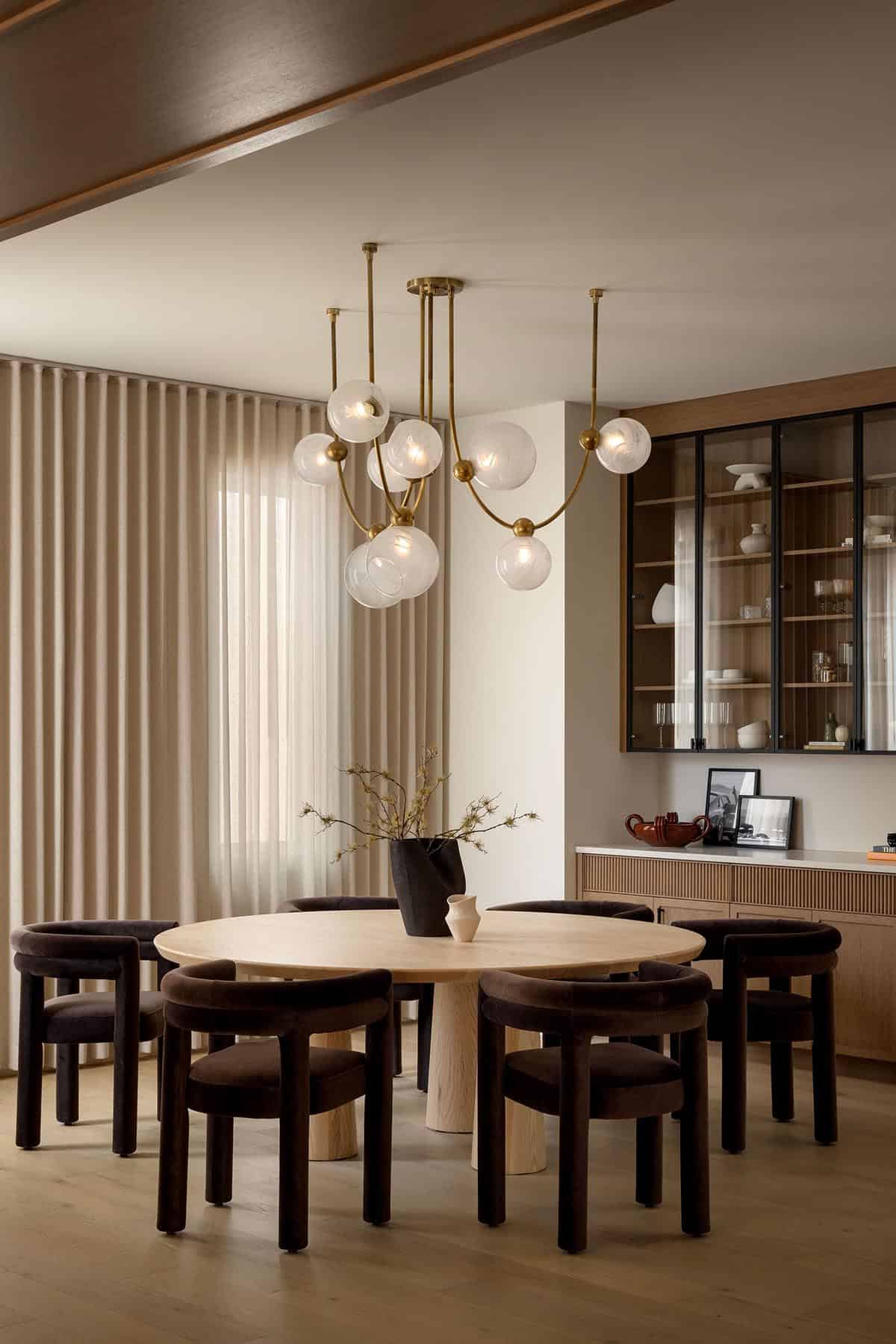 Dining area with round wood table, brown velvet chairs, and bubble-glass chandelier