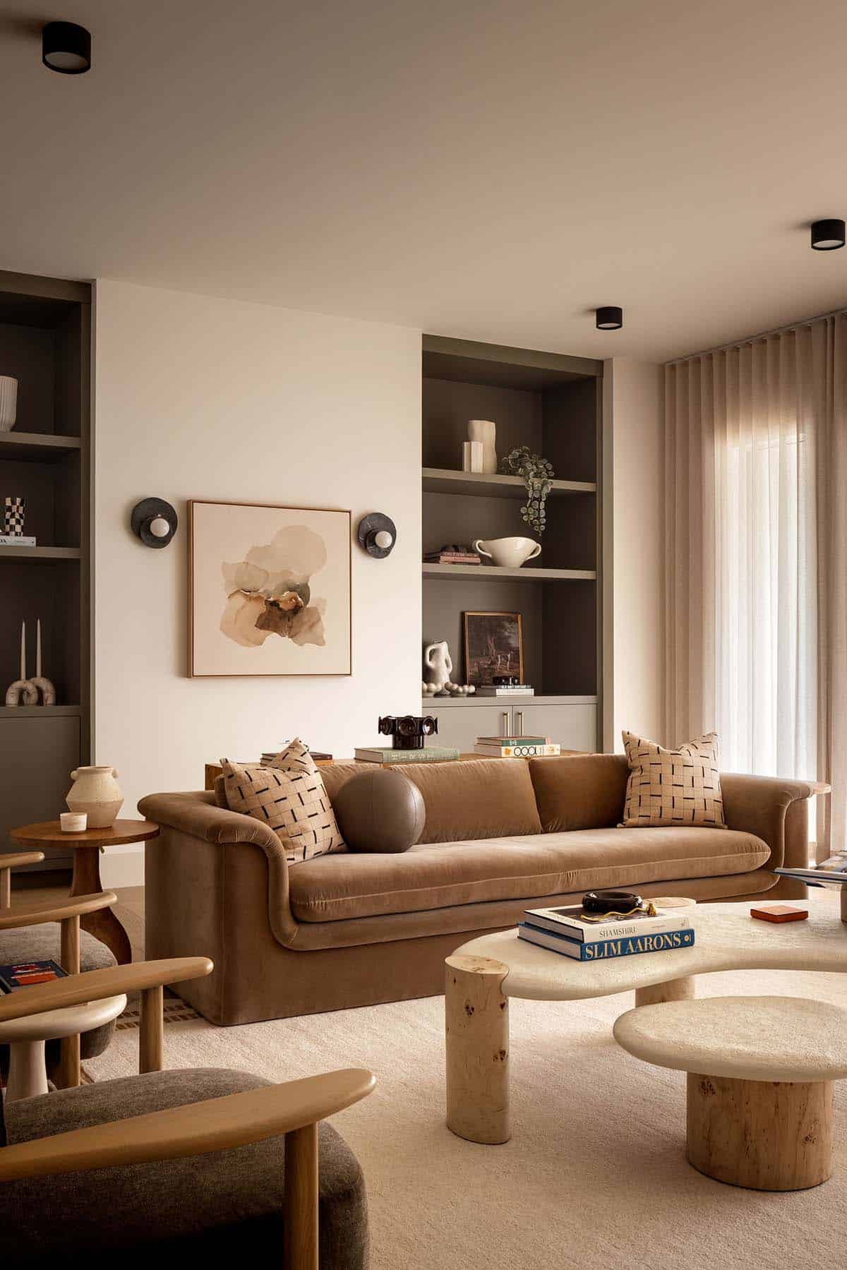 Living room with camel velvet sofa, built-in shelving, and round stone coffee tables