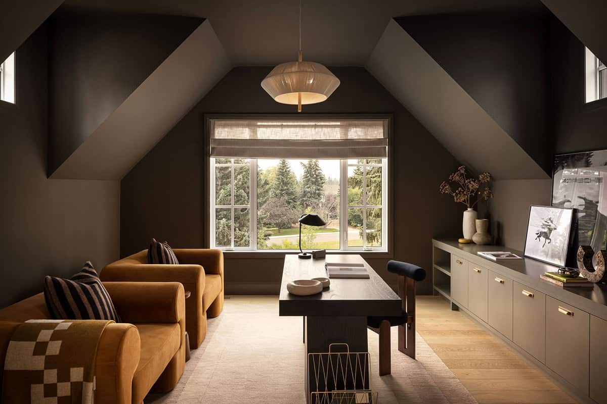 Dark attic home office with vaulted ceiling, mustard armchairs, and desk by window