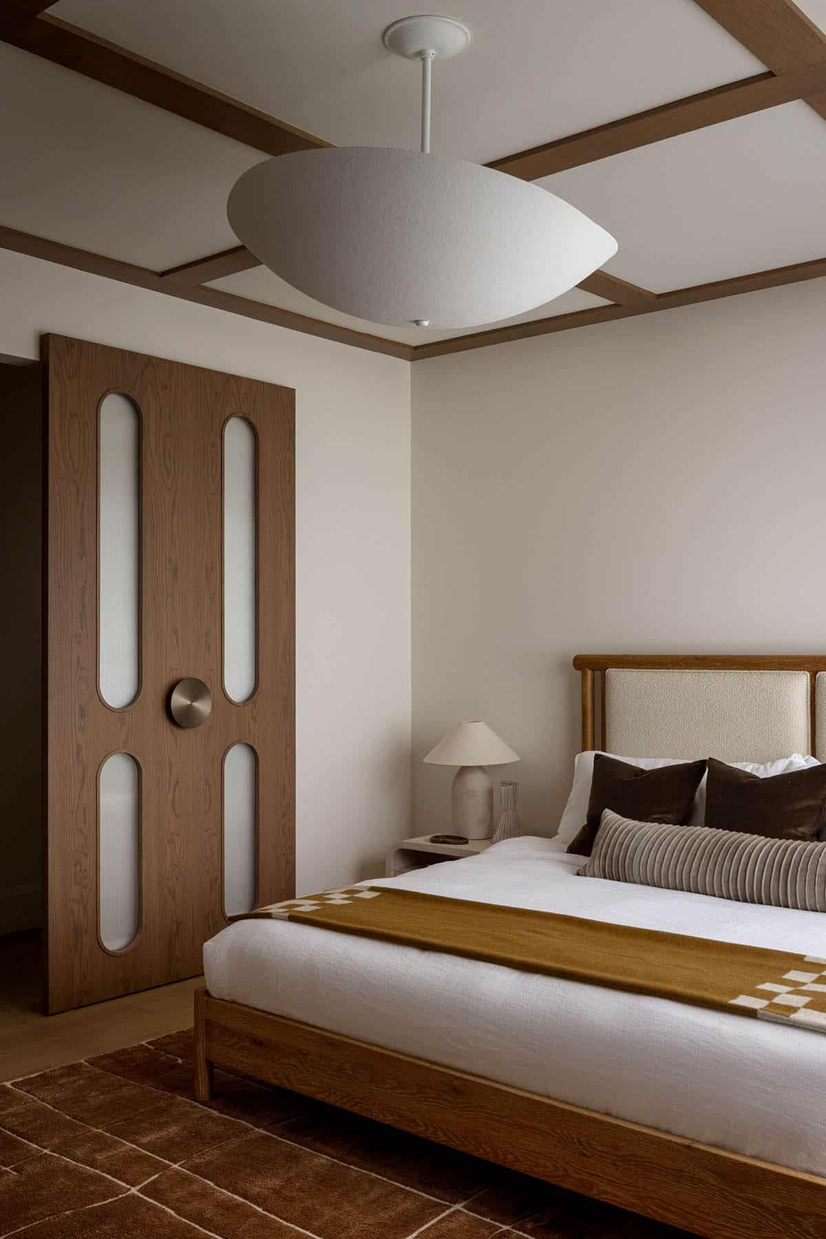 Bedroom with coffered ceiling, oval pendant light, and reeded-glass wood door