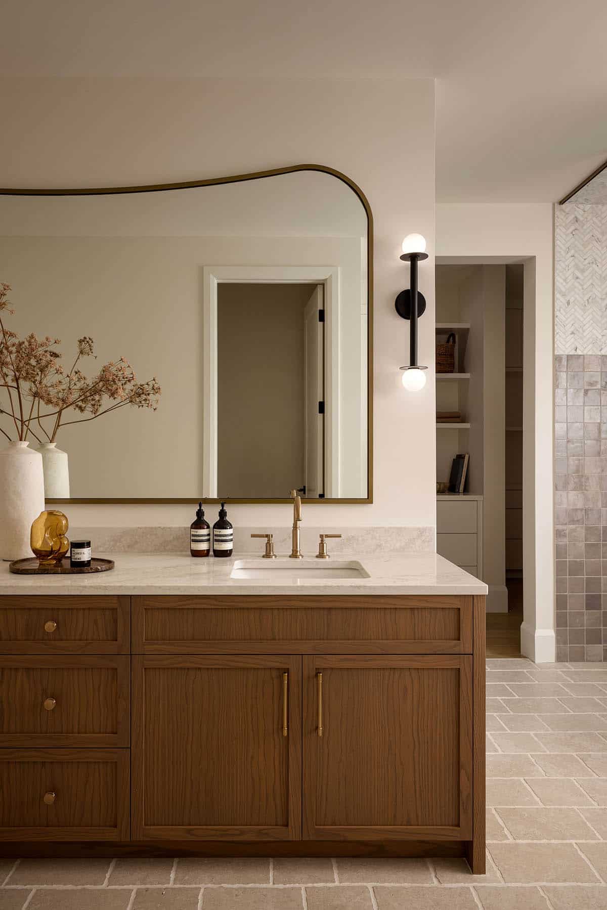 Bathroom vanity with curved brass-trimmed mirror and black wall sconce