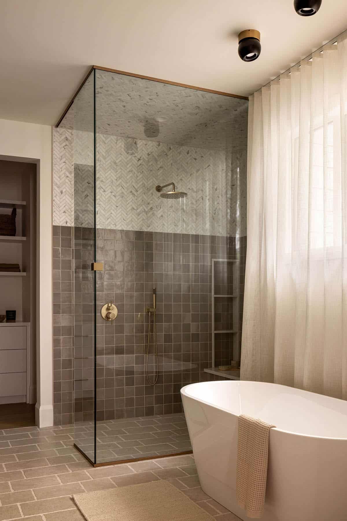 Glass-enclosed shower with herringbone marble and gray zellige tile