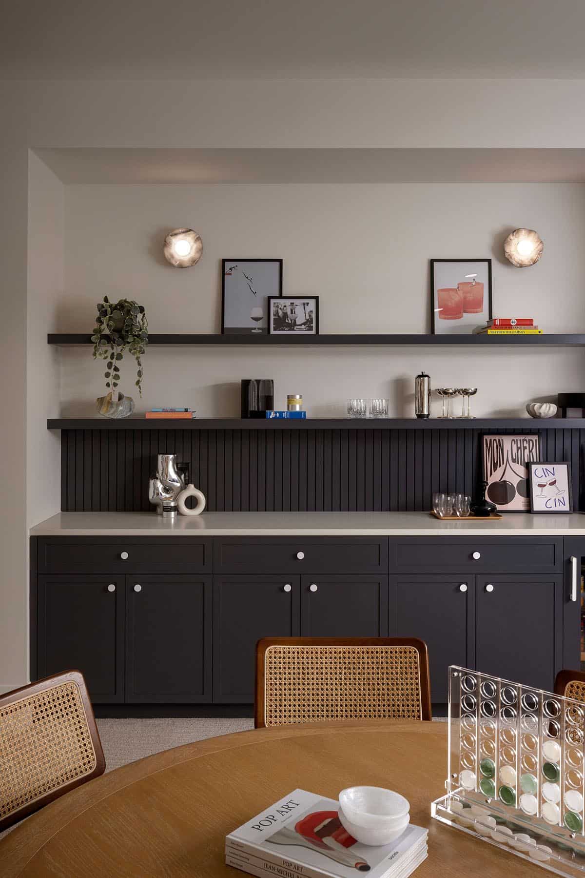 Wet bar with charcoal cabinetry, open shelving, and rattan dining chairs