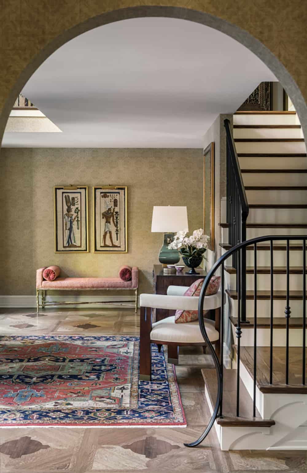 Curved staircase beside vintage rug and Egyptian-motif wall art