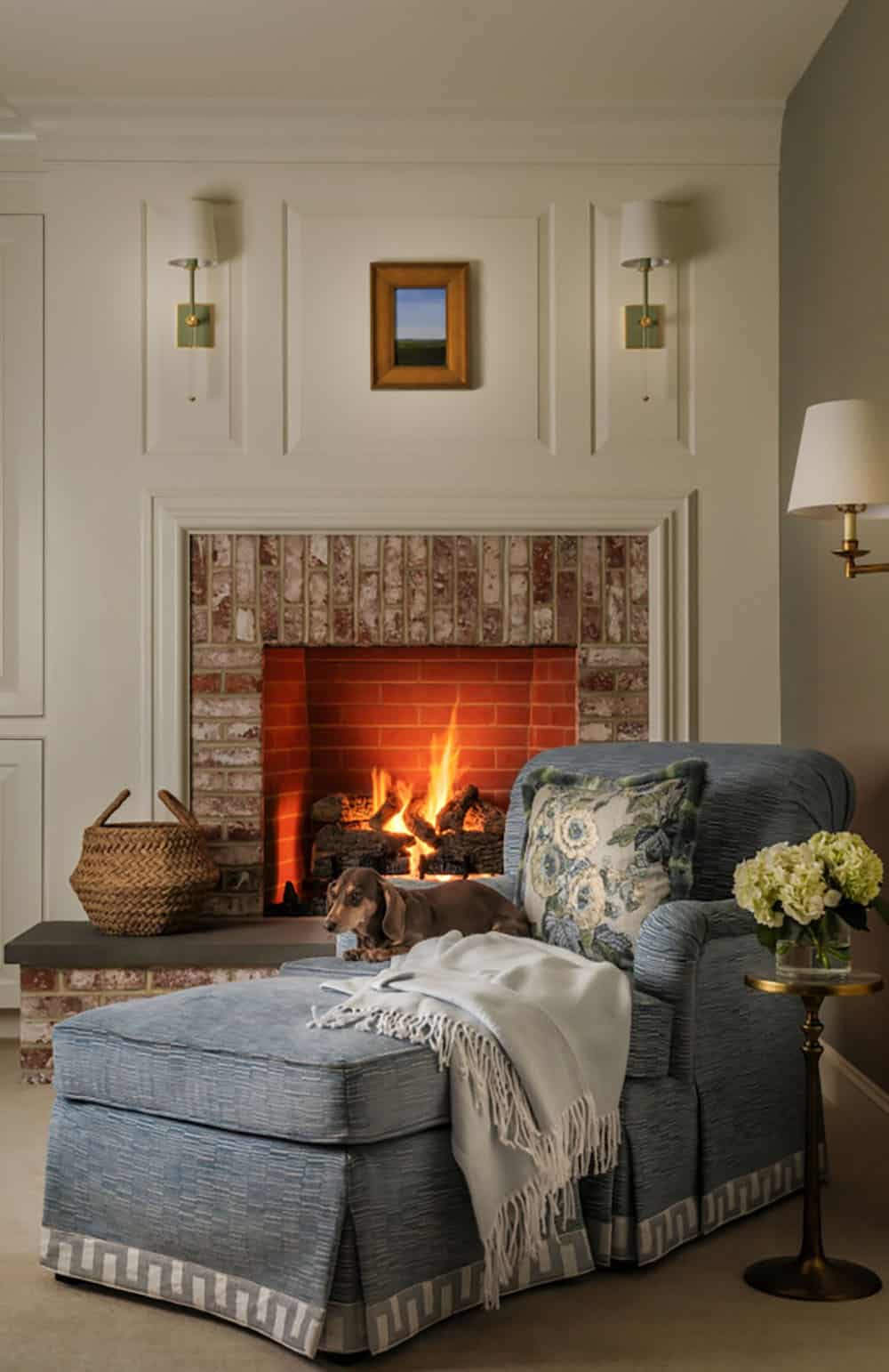 Blue chaise chair beside brick fireplace with resting dachshund