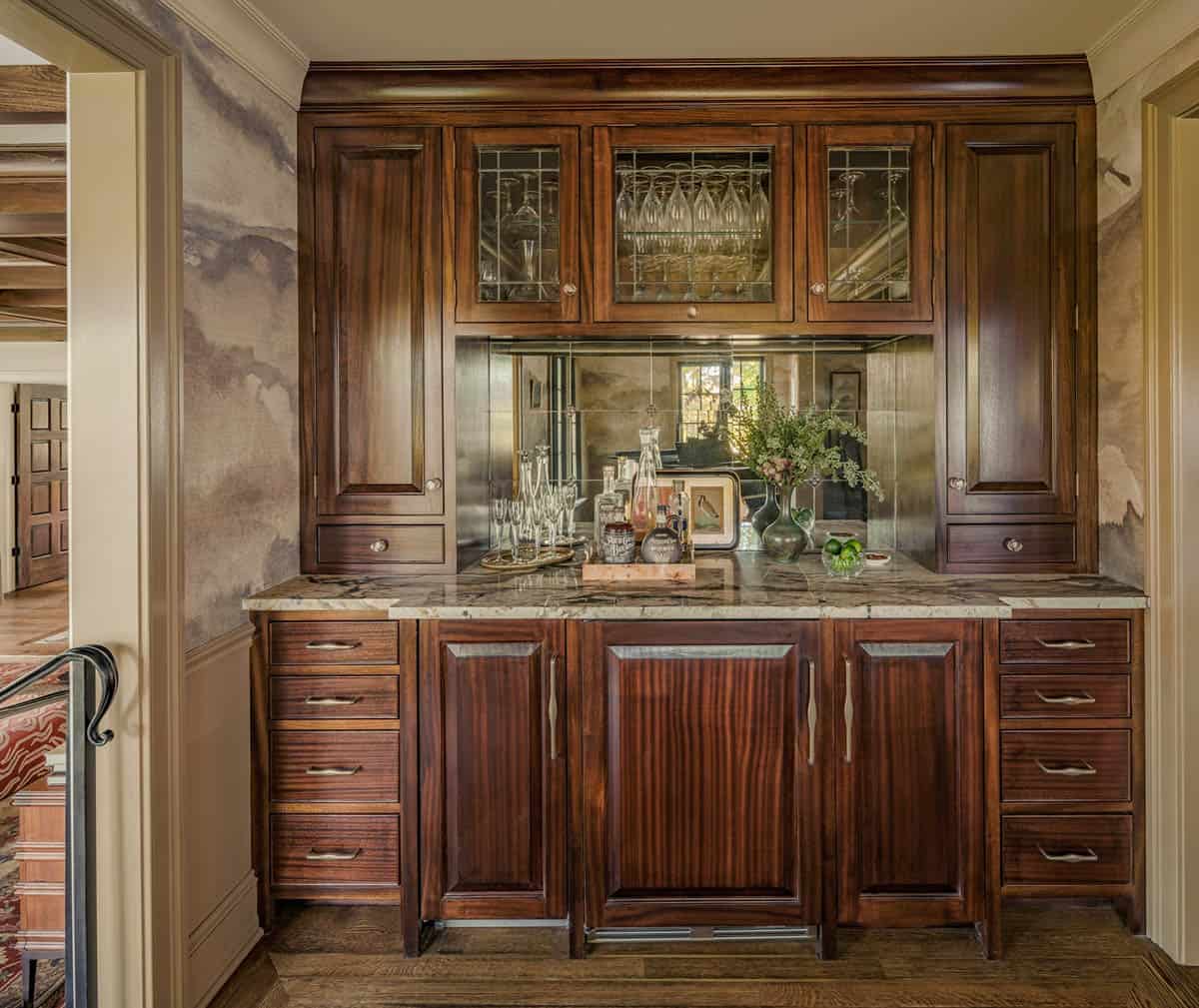 Wet bar with mirrored backsplash and stone countertop between cabinets