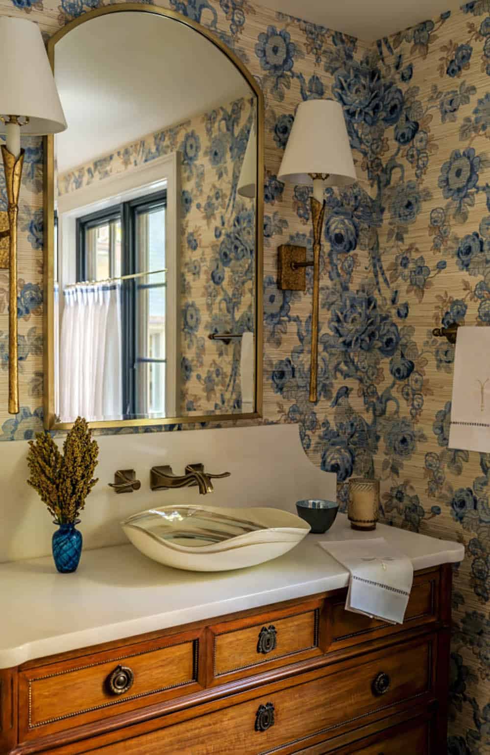 Floral wallpaper powder room with sculptural sink and arched mirror