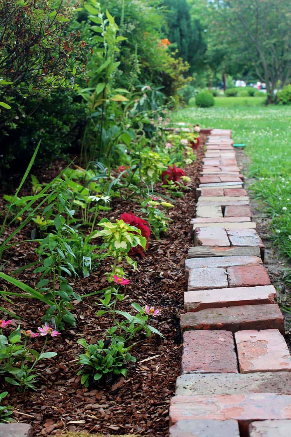 Reclaimed bricks laid flat in an irregular row to edge a mulched flower bed alongside a lawn