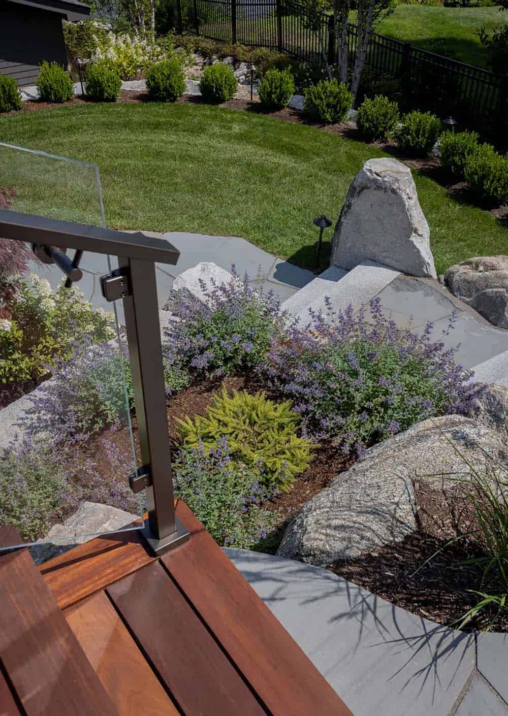 Stone steps and glass railing beside a landscaped garden bed