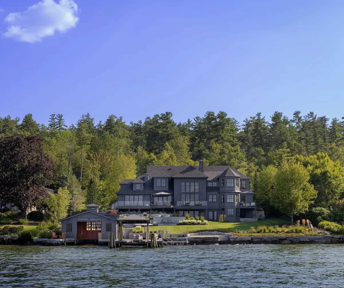 Distant view of the gray shingle-style home from across the lake