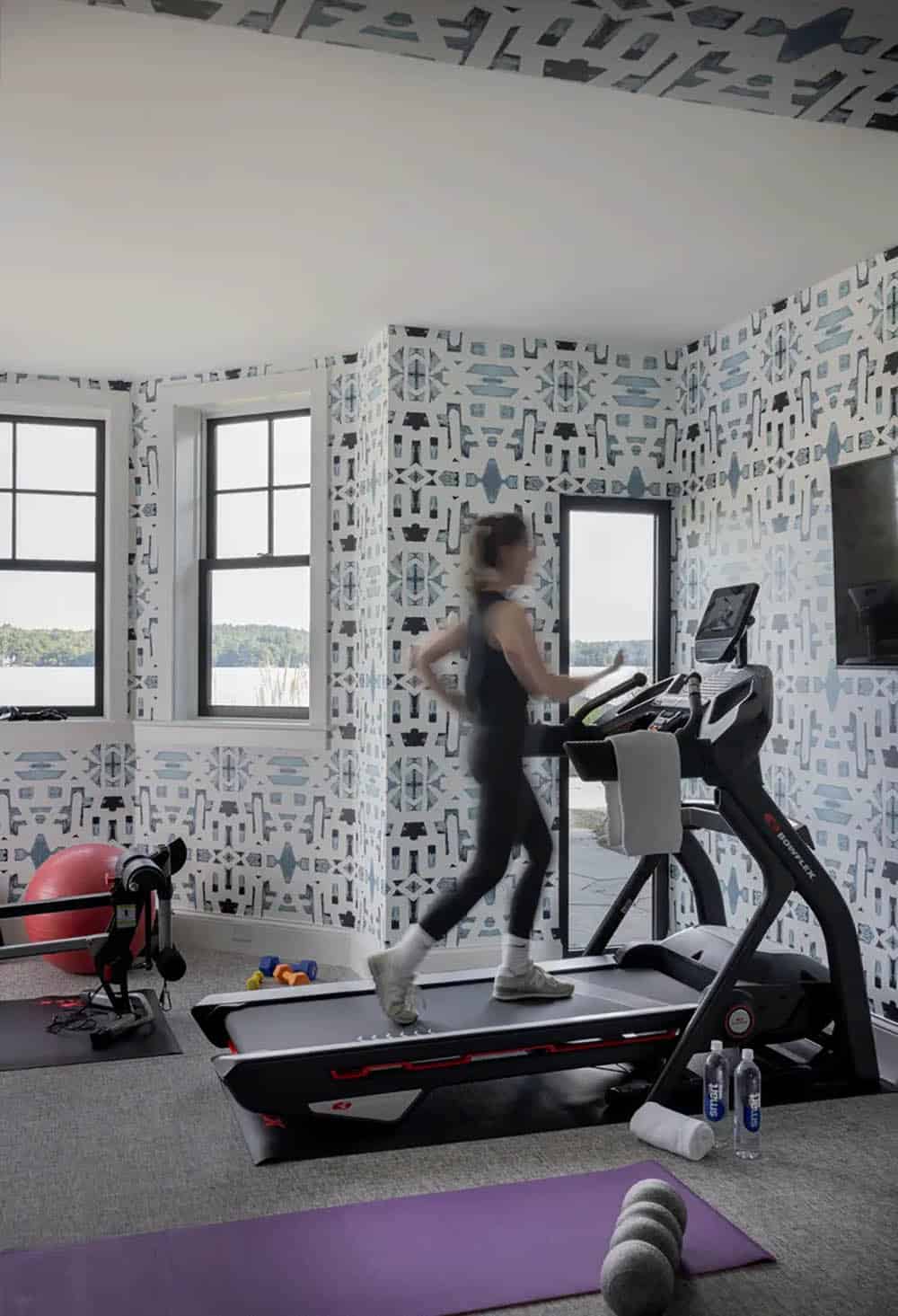 Home gym with patterned wallpaper, treadmill, and lake view windows