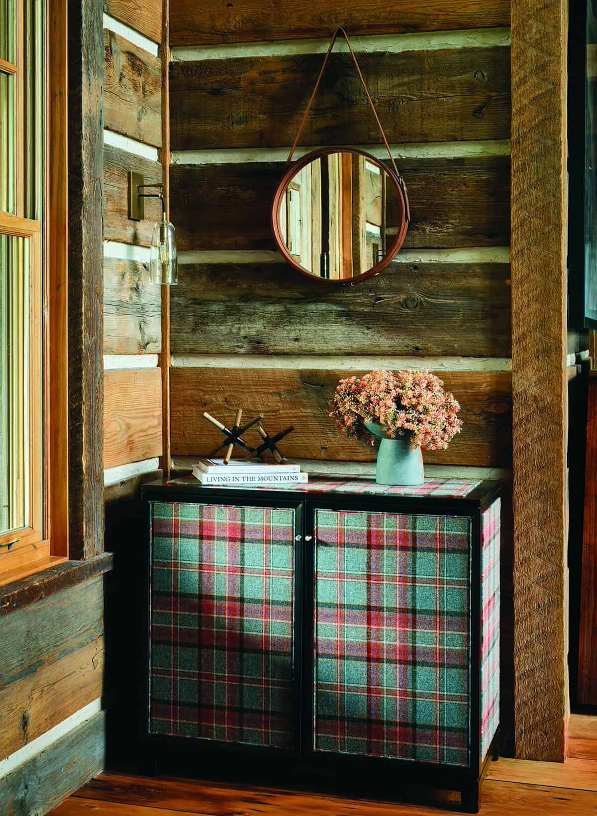 Round leather mirror above plaid cabinet in log cabin entryway