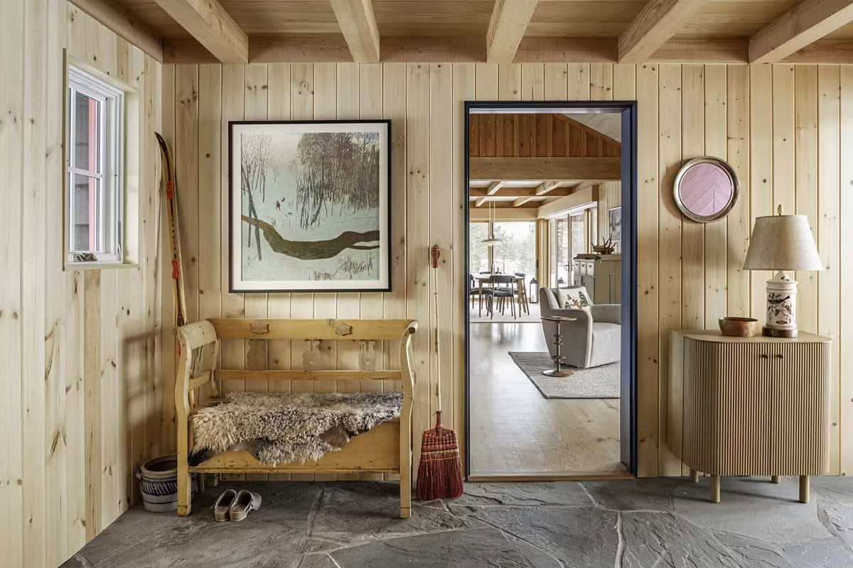 Wood-paneled mudroom with bench, artwork, and view into living area