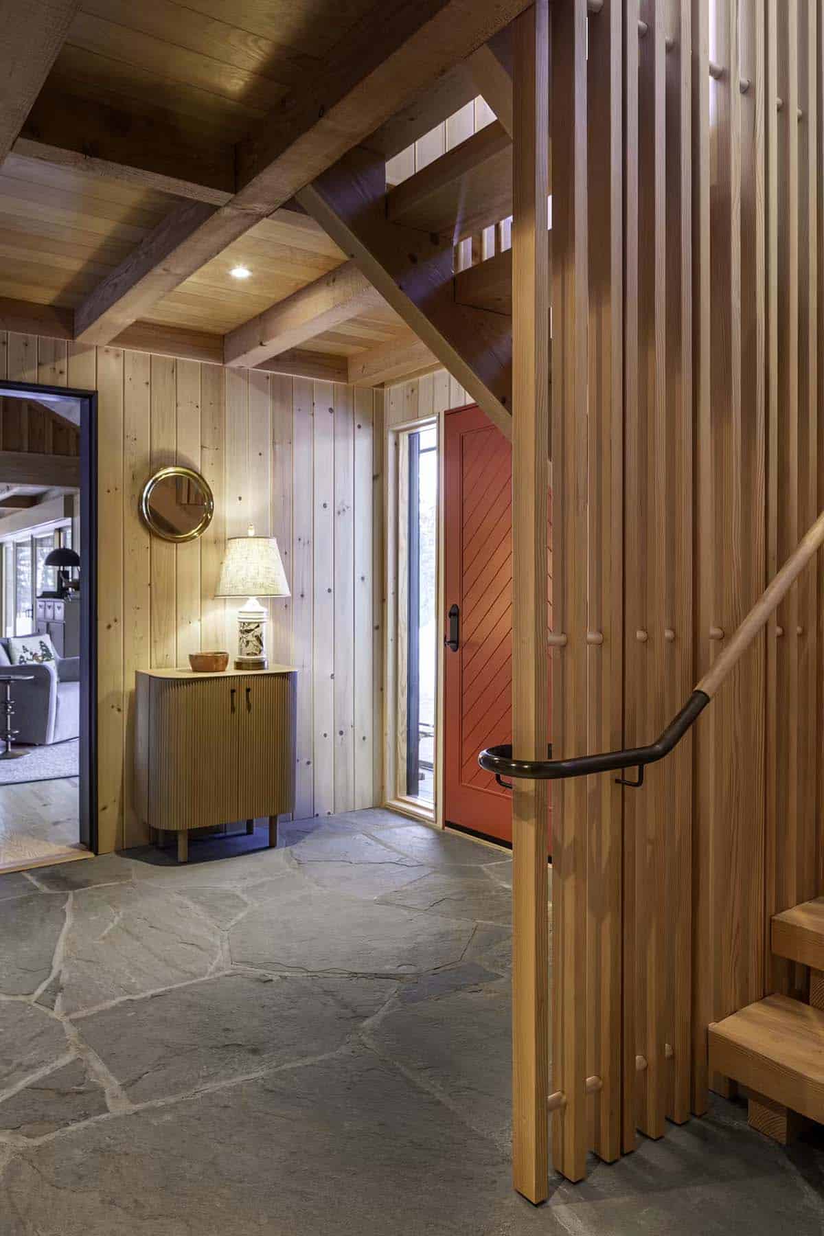 Foyer with wood slat staircase, red door, and small cabinet