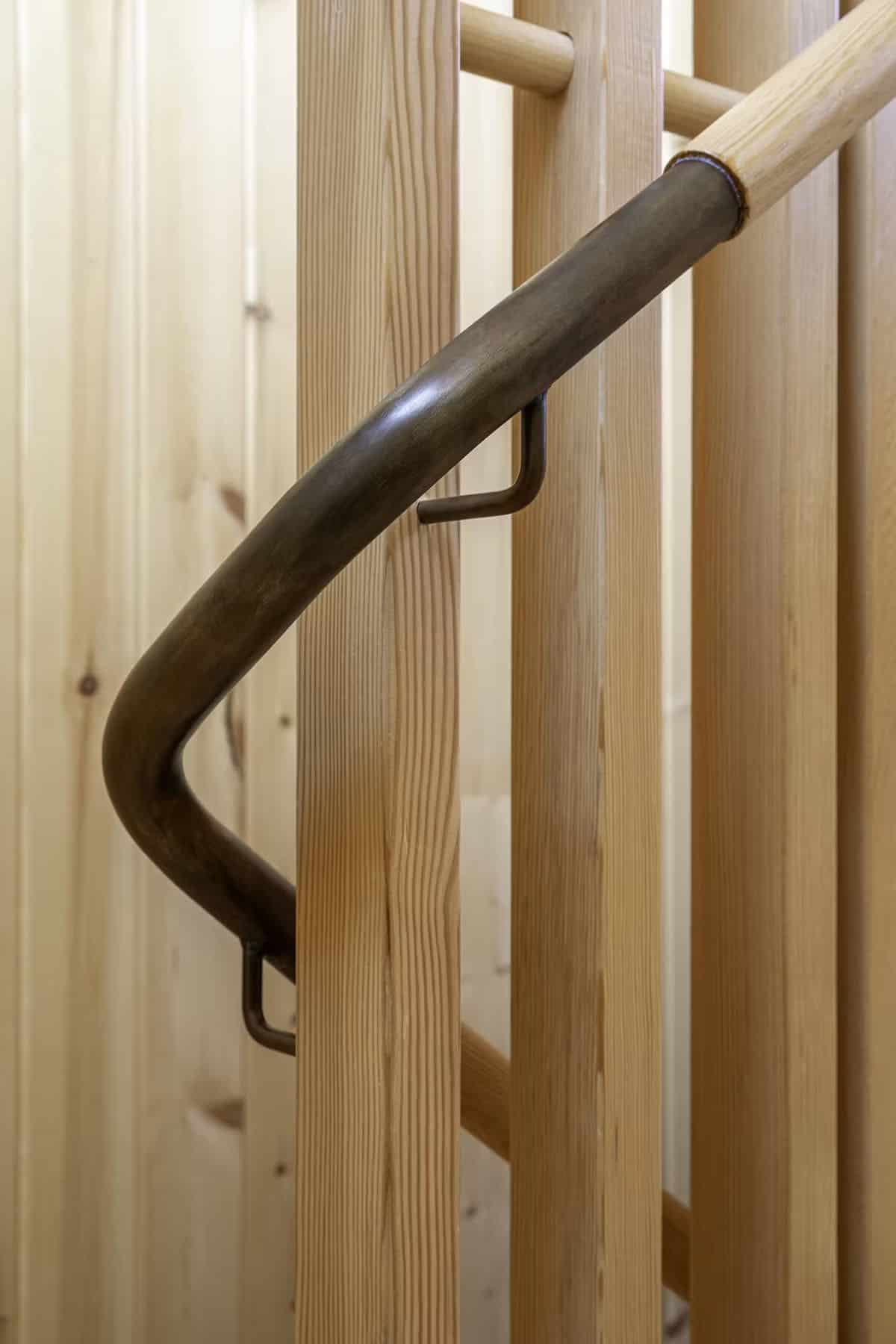 Detail of curved bronze handrail bracket on wood post