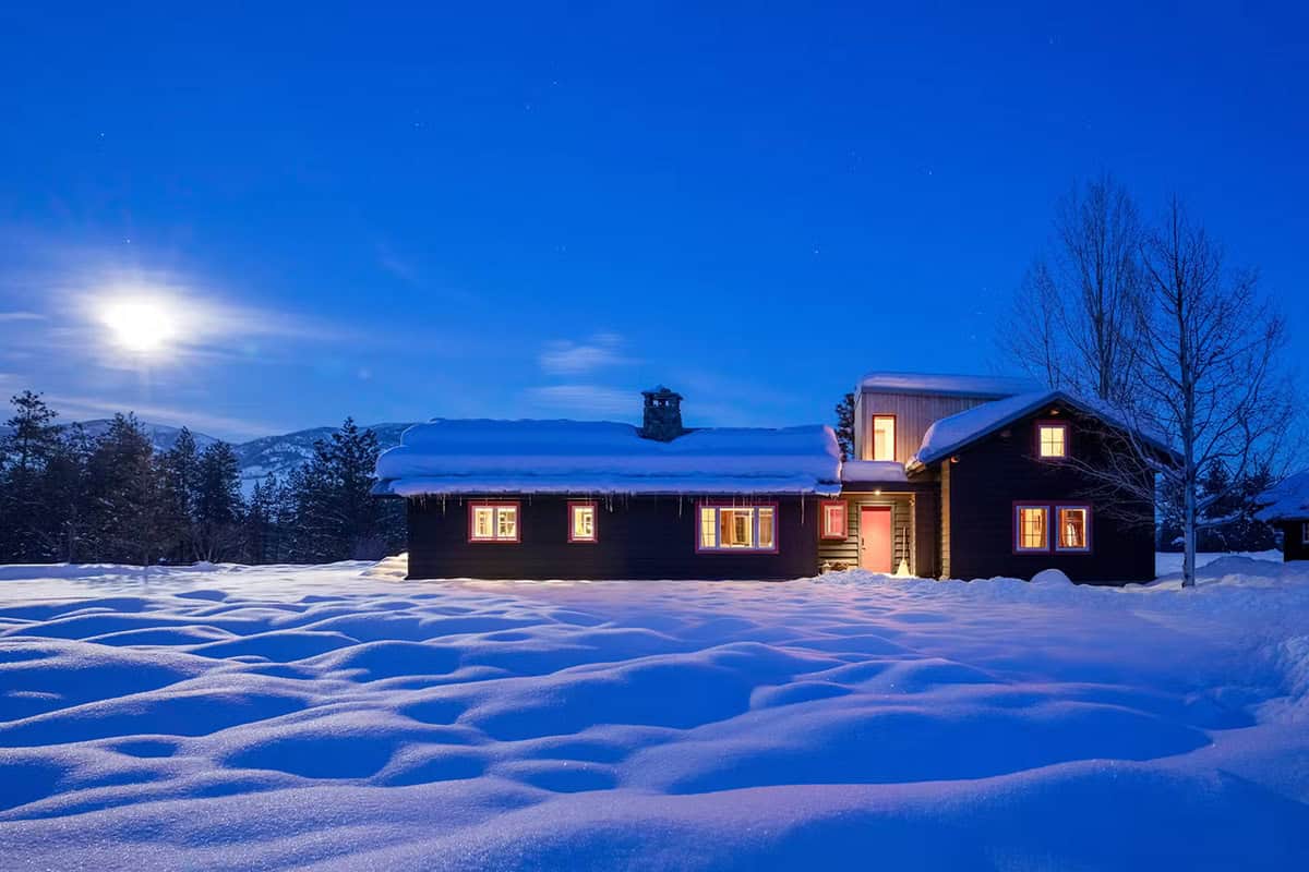 Cabin illuminated at night under moonlit sky with snowy field