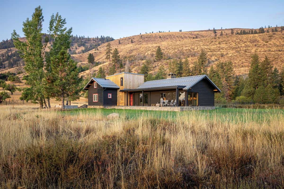 Black cabin with wood addition surrounded by golden grasses and hillside in fall