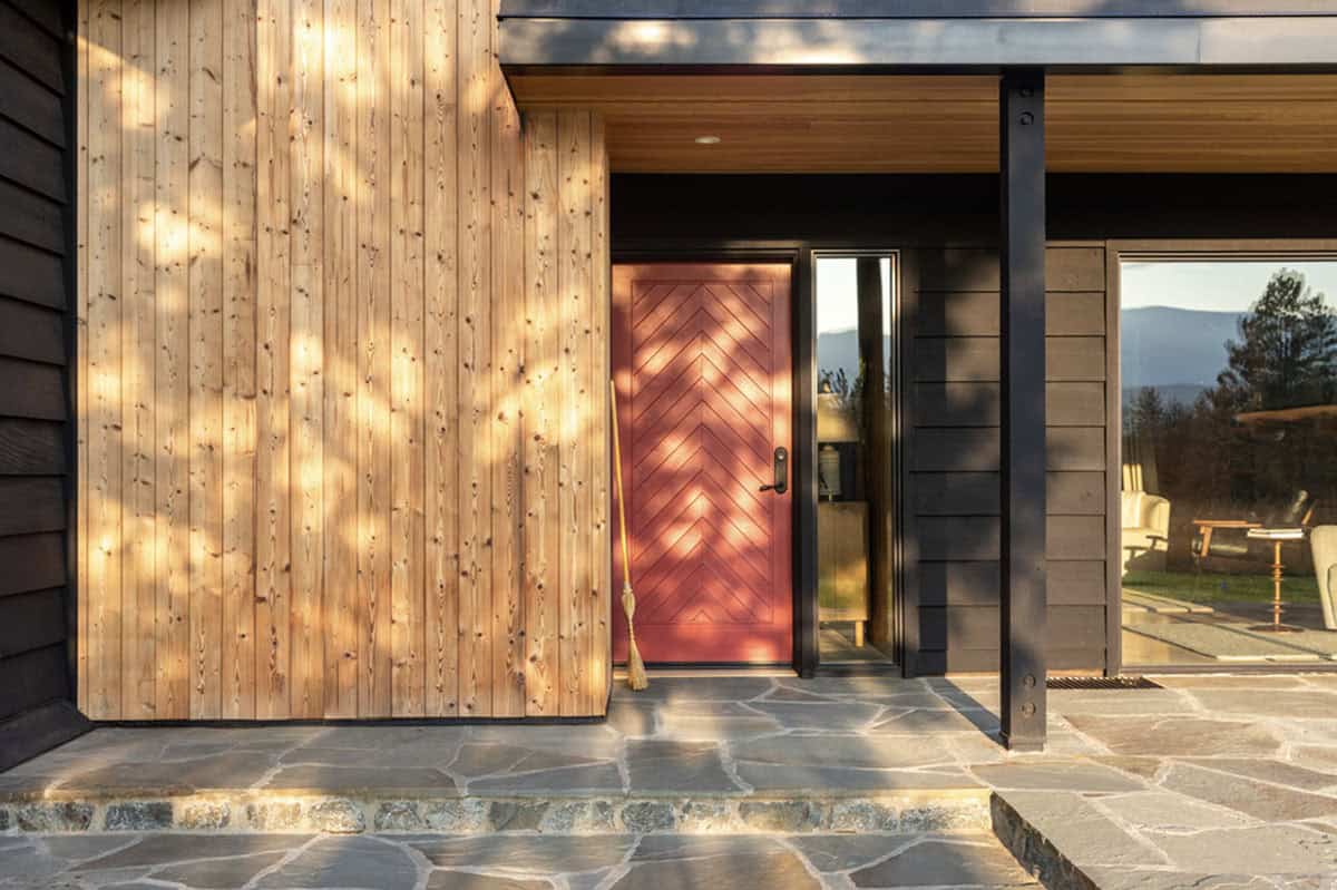 Red front door framed by wood siding and covered black steel porch