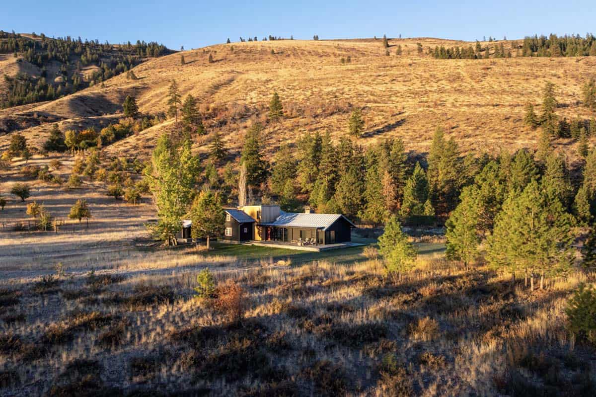 Aerial view of cabin nestled among pines on golden hillside